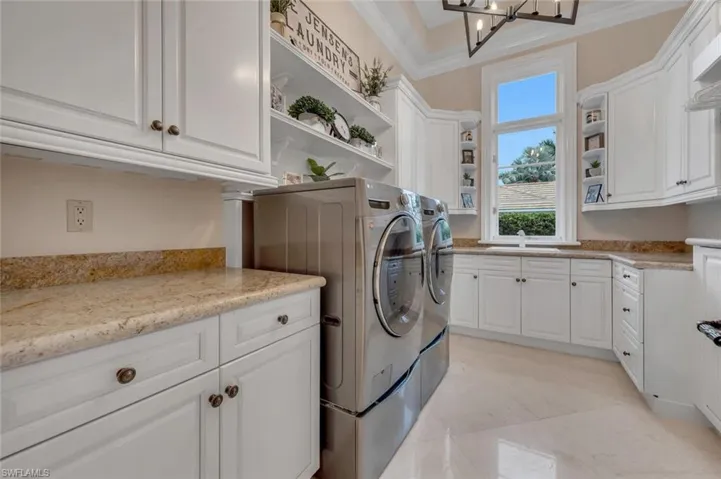 Laundry room featuring cabinet space, washing machine and dryer, crown molding, and a chandelier