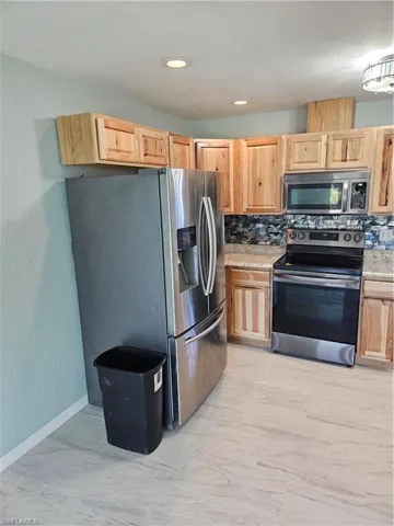 Kitchen featuring stainless steel fridge with ice dispenser, light brown cabinets, range, and backsplash