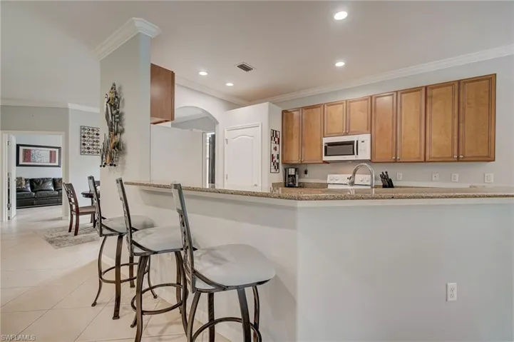 Kitchen with a kitchen bar, crown molding, light stone countertops, light tile patterned floors, and white appliances