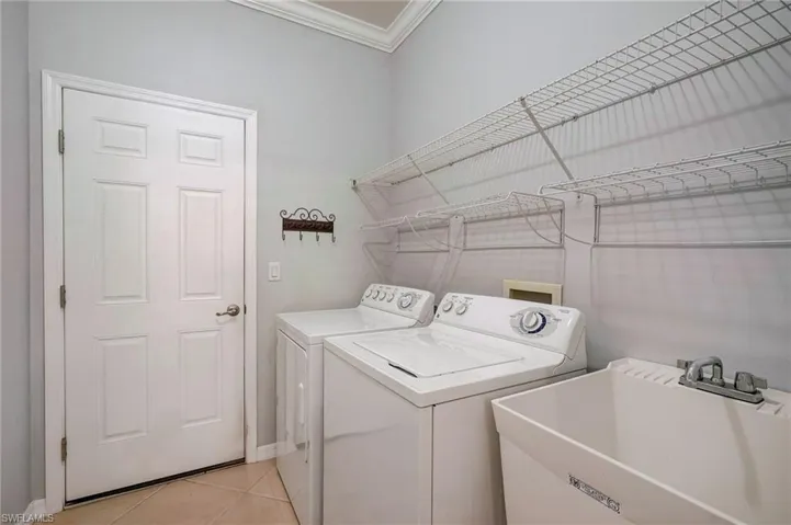 Laundry room featuring light tile patterned floors, sink, crown molding, and washer and clothes dryer