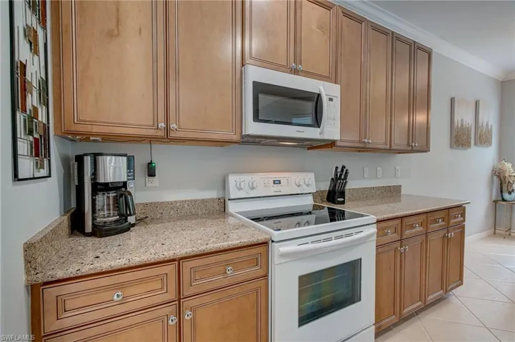 Kitchen with white appliances, crown molding, light tile patterned flooring, and light stone counters
