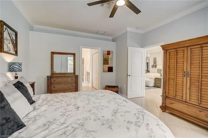 Tiled bedroom with ceiling fan, ornamental molding, and ensuite bath