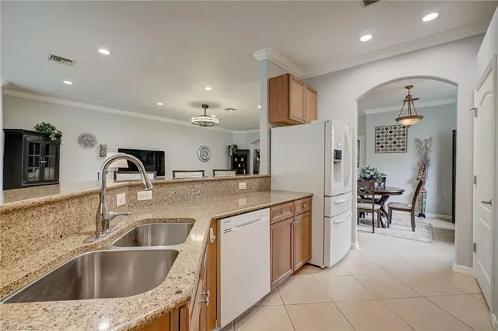 Kitchen with crown molding, light stone counters, white appliances, and light tile patterned floors