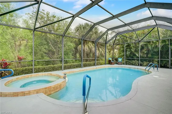 View of swimming pool featuring glass enclosure, an in ground hot tub, and a patio area