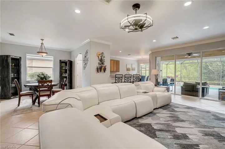 Living room with light tile patterned flooring, ceiling fan with notable chandelier, plenty of natural light, and ornamental molding