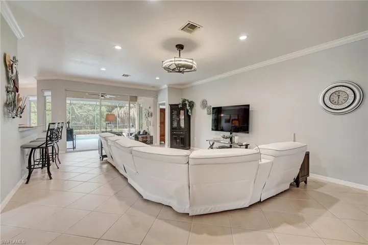 Living room featuring light tile patterned floors, ceiling fan with notable chandelier, and crown molding