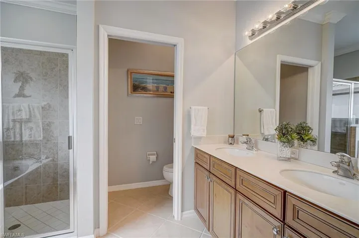 Bathroom featuring ornamental molding, tile patterned floors, tiled shower, double sink vanity, and toilet