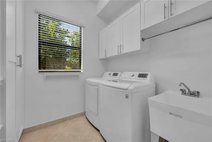 Spacious laundry room with abundant cabinetry, utility sink, and window providing natural light.