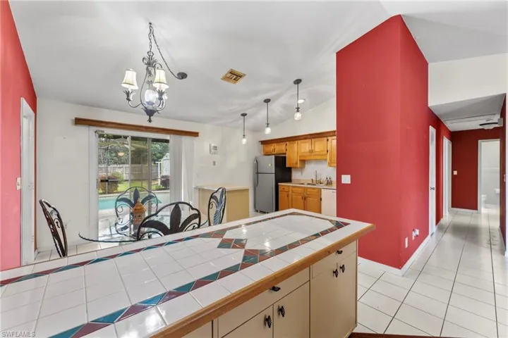 Kitchen with light tile patterned floors, visible vents, tile countertops, freestanding refrigerator, and white dishwasher
