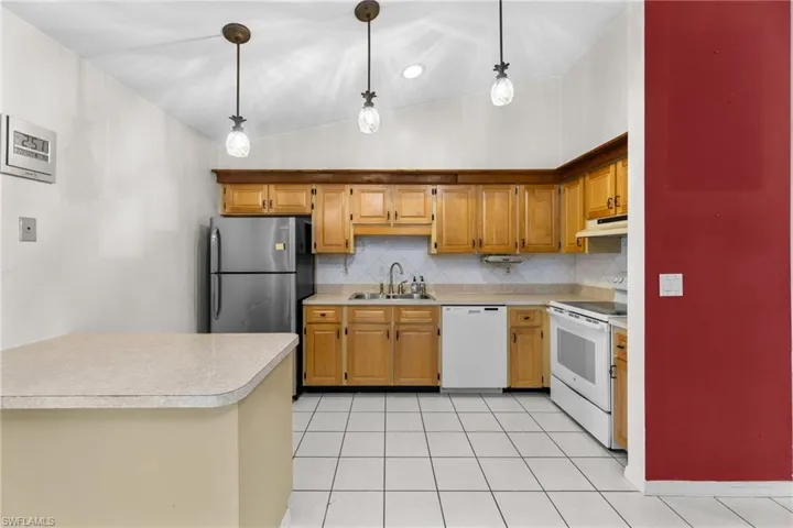 Kitchen featuring a sink, white appliances, pendant lighting, and light countertops