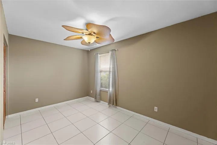 Empty room with light tile patterned floors, ceiling fan, and baseboards