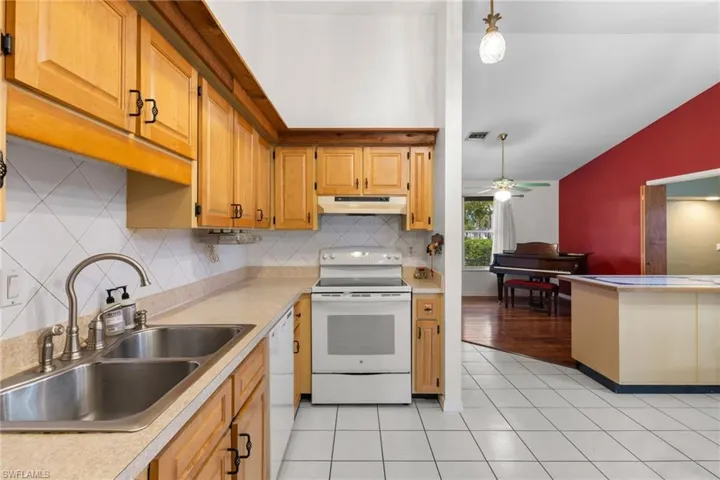 Kitchen with white appliances, vaulted ceiling, light countertops, under cabinet range hood, and a sink