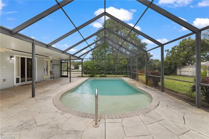 Outdoor pool with glass enclosure, a patio area, and fence