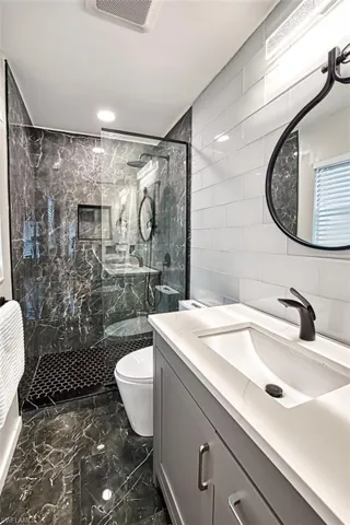 Bathroom with tile walls, a marble finish shower, vanity, and marble finish floors