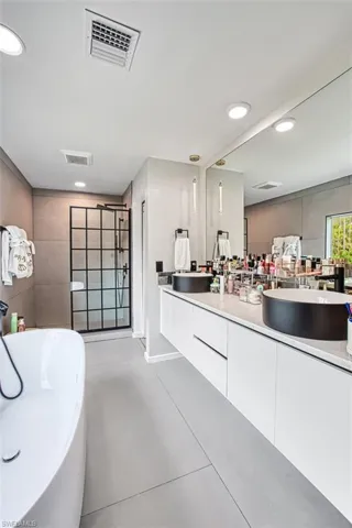Bathroom featuring double vanity, a soaking tub, recessed lighting, and a tile shower