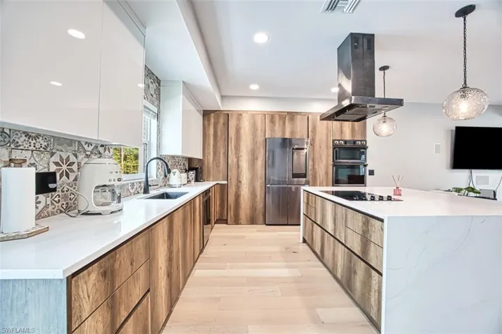 Kitchen featuring black appliances, modern cabinets, island exhaust hood, light wood finished floors, and a spacious island