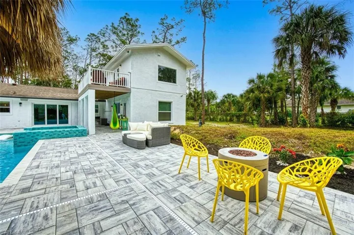 Rear view of house with a patio area, a balcony, an outdoor pool, a hot tub, and stucco siding