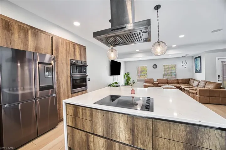 Kitchen with black appliances, wall chimney exhaust hood, light wood-style floors, recessed lighting, and open floor plan