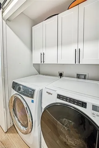 Washroom with cabinet space, washer and dryer, and light wood finished floors