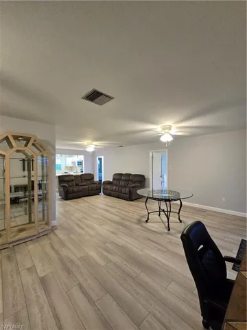 Living room with a textured ceiling, ceiling fan, and light wood-type flooring
