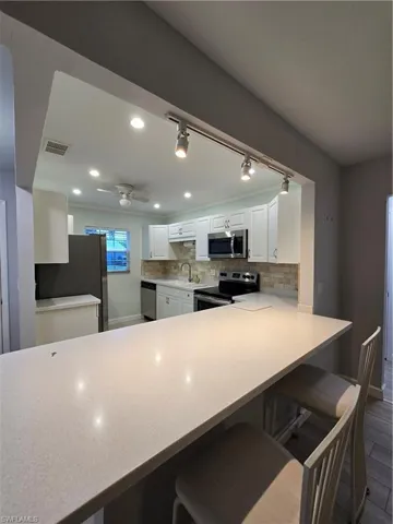 Kitchen featuring appliances with stainless steel finishes, white cabinetry, ceiling fan, dark wood-type flooring, and a kitchen breakfast bar