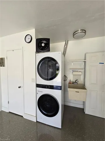 Clothes washing area featuring a textured ceiling, sink, and stacked washing maching and dryer