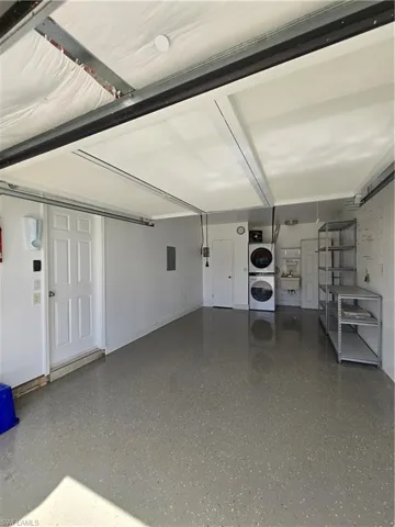 Garage featuring electric panel and stacked washing maching and dryer