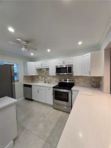 Kitchen with crown molding, white cabinetry, light tile patterned floors, ceiling fan, and appliances with stainless steel finishes