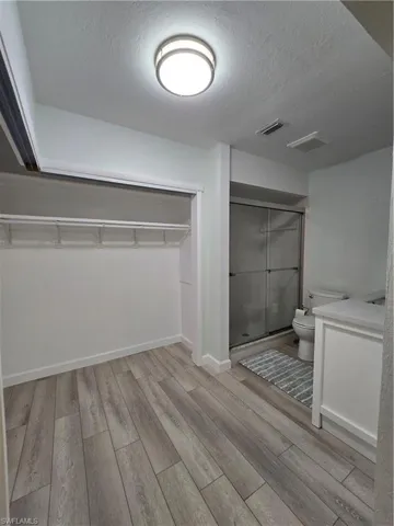 Bathroom featuring toilet, wood-type flooring, an enclosed shower, and a textured ceiling