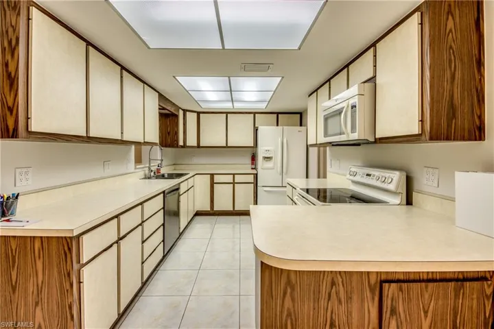 Kitchen with white appliances, a peninsula, light tile patterned floors, and light countertops