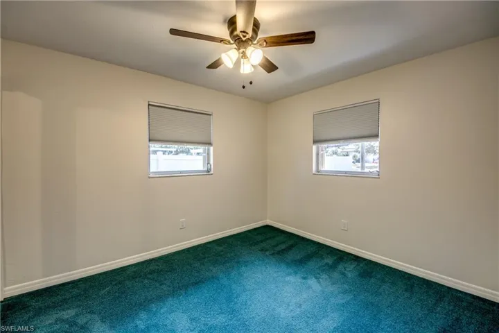 Empty room featuring plenty of natural light, a ceiling fan, and dark colored carpet