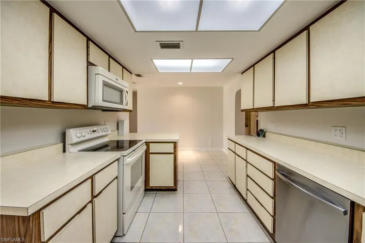 Kitchen featuring white appliances, light countertops, a peninsula, light tile patterned flooring, and light wood finish cabinetry