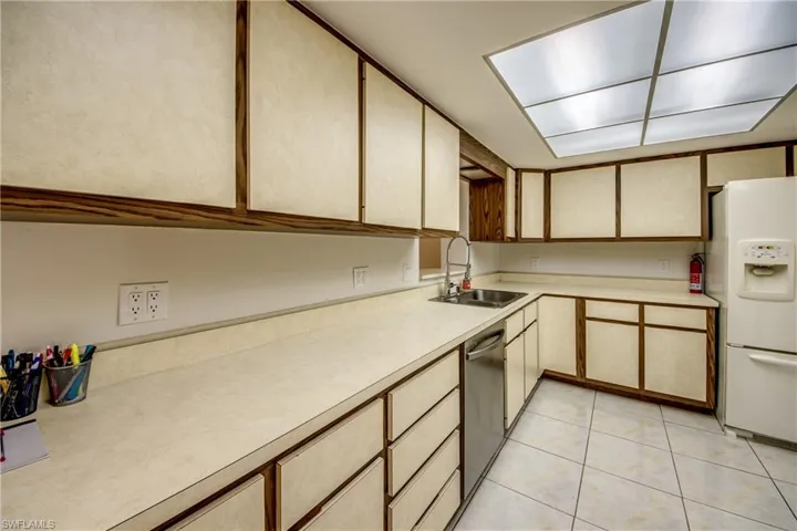 Dual tone kitchen with light countertops, white refrigerator with ice dispenser, dishwasher, light tile patterned floors, and dual tone cabinetry