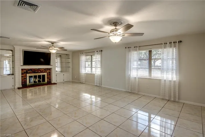 Unfurnished living room featuring light tile patterned floors, a brick fireplace, and a ceiling fan