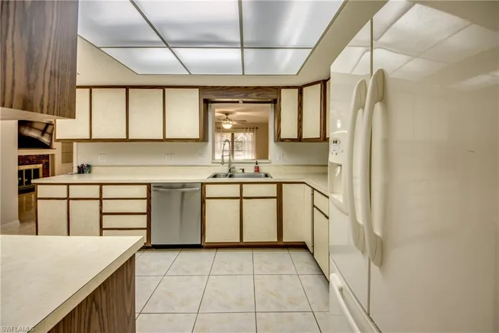 Dual tone kitchen with white fridge with ice dispenser, light countertops, stainless steel dishwasher, light tile patterned floors, and ceiling fan