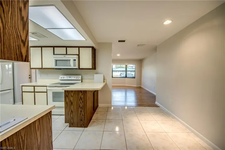 Kitchen with a peninsula, wood finish cabinetry, white appliances, light countertops, and recessed lighting
