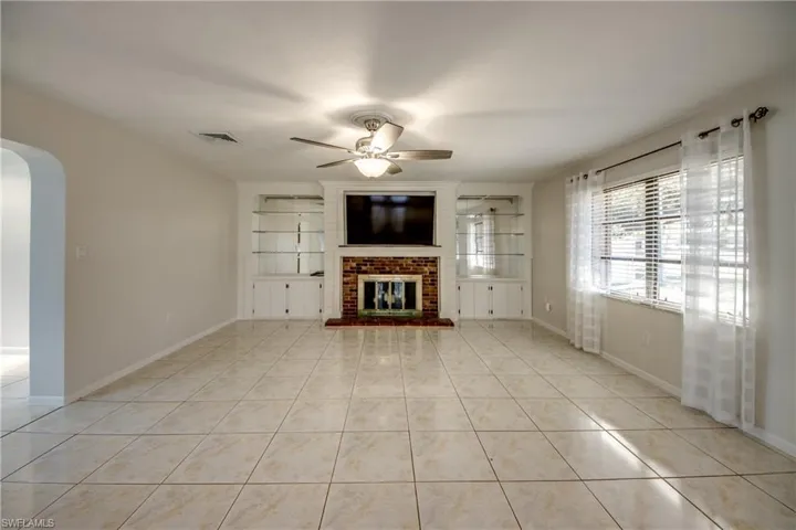 Unfurnished living room featuring arched walkways, ceiling fan, light tile patterned floors, and a brick fireplace