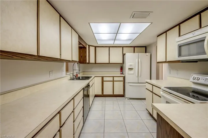 Kitchen with white appliances, light countertops, light wood finish cabinets, and light tile patterned floors
