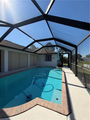 Outdoor pool with glass enclosure, a sunroom, and a patio