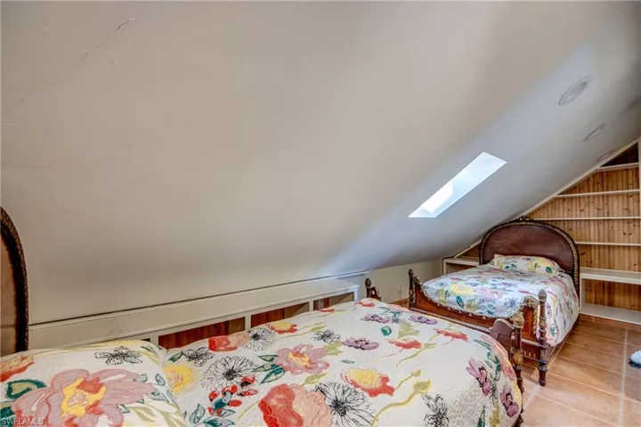 Bedroom with vaulted ceiling with skylight, wooden walls, and tile patterned flooring
