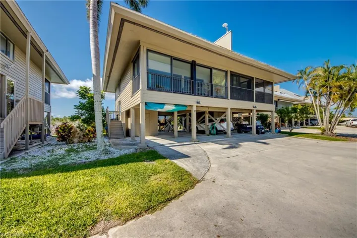 View of front facade featuring driveway, a sunroom, stairway, a front lawn, and a carport