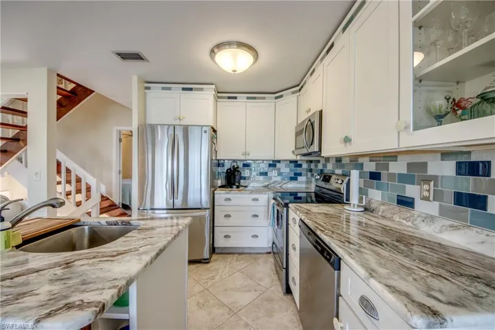Kitchen with stainless steel appliances, decorative backsplash, white cabinetry, a sink, and light stone countertops