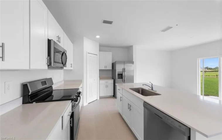 Well appointed kitchen featuring white shaker cabinets, quartz countertops, stainless steel appliances including a range, microwave, dishwasher and refrigerator with ice maker, a center island with sink and a pantry closet — all bathed in natural light with backyard views.