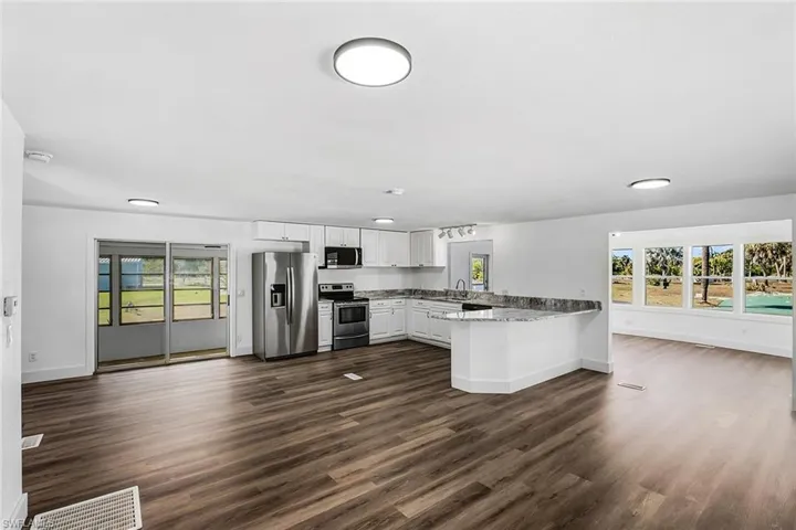 Open-concept living space with wood-finish flooring, white cabinetry, stainless steel appliances, and a granite-look countertop island