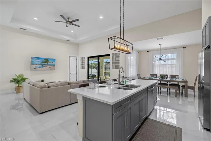 Kitchen with light tile patterned flooring, sink, an island with sink, a tray ceiling, and hanging light fixtures