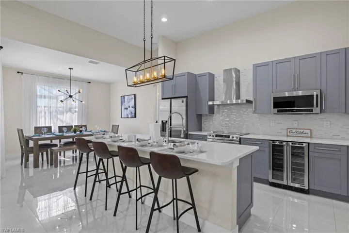 Kitchen with stainless steel appliances, wall chimney exhaust hood, wine cooler, an island with sink, and light tile patterned floors