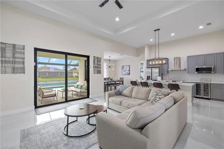 Tiled living room featuring sink, a high ceiling, ceiling fan with notable chandelier, a tray ceiling, and beverage cooler