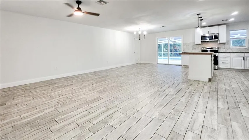 Kitchen with open floor plan, white cabinets, a ceiling fan, a kitchen island, and stainless steel appliances