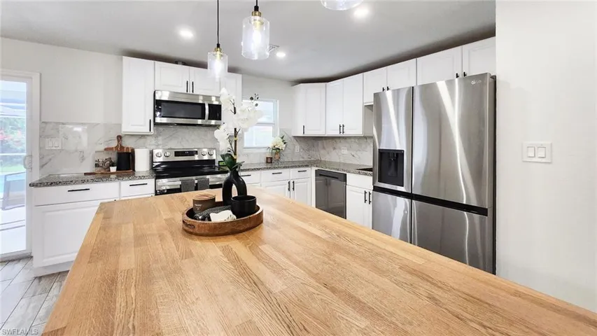 Kitchen featuring stainless steel appliances, wooden counters, decorative light fixtures, and white cabinets