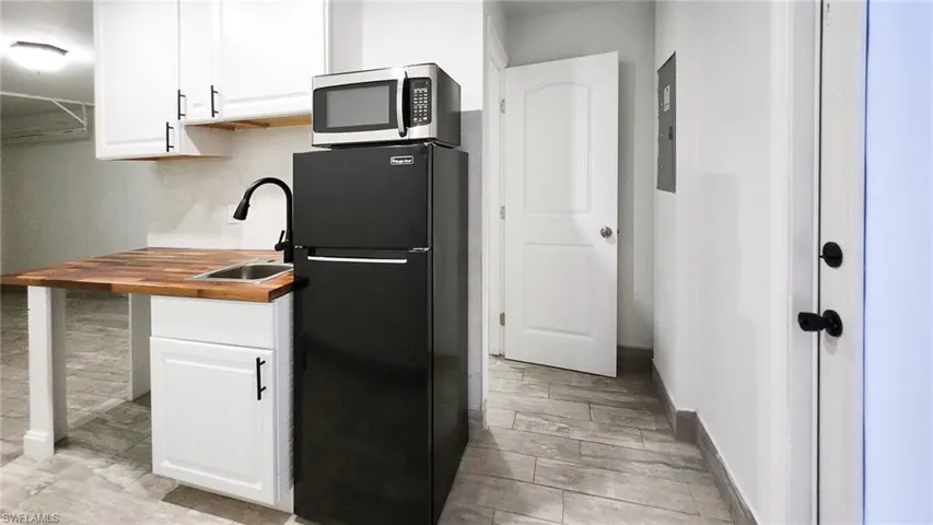 Kitchen with freestanding refrigerator, wood counters, white cabinetry, stainless steel microwave, and light wood-type flooring